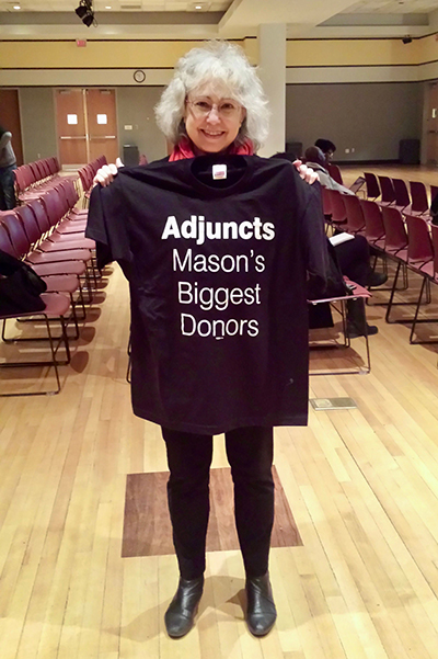 A woman holds up a black T-shirt that says Adjuncts Mason’s Biggest Donors.