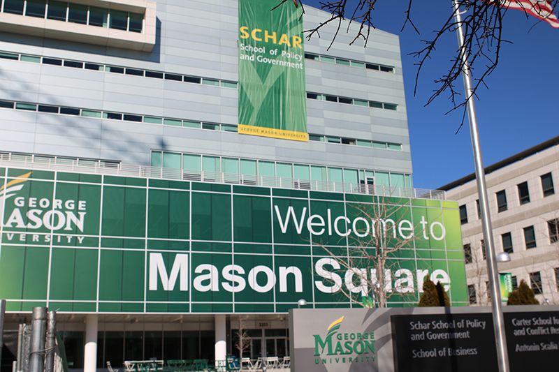 A silver and glass building has a green Schar School banner on it.
