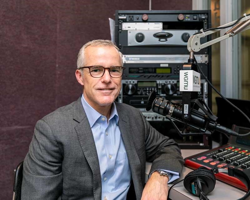 A man in a blue shirt, gray jacket, and wearing glasses sits before a WGMU microphone.