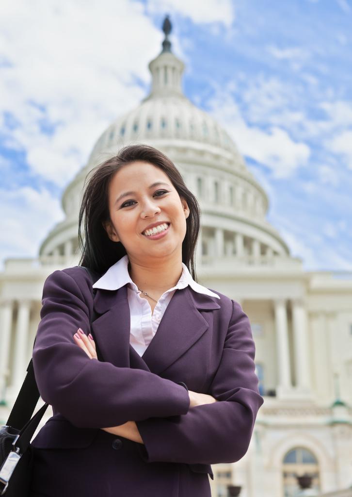 A woman in professional attire smiling at the camera in front of the U.S. Capitol Building.