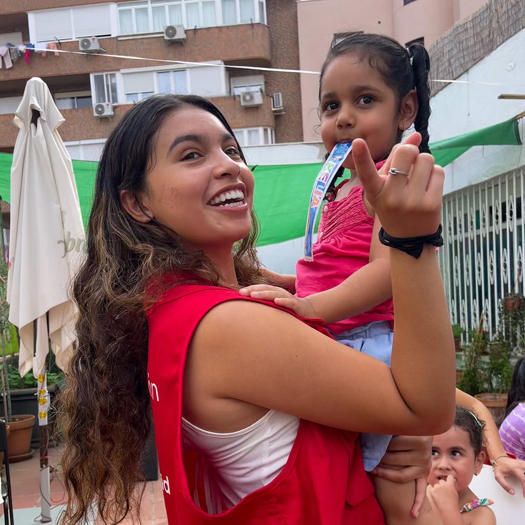 Gabriela Manzanares wearing a red vest and smiling while holding a young child.