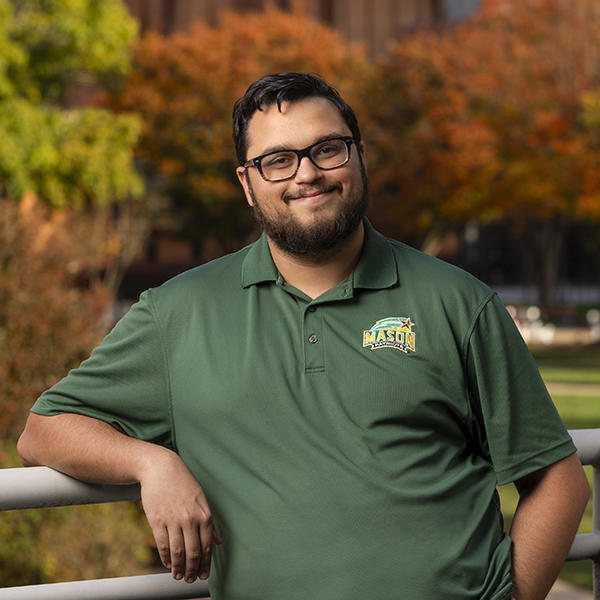 Zayd Hamid stands outside smiling while wearing a green George Mason University shirt