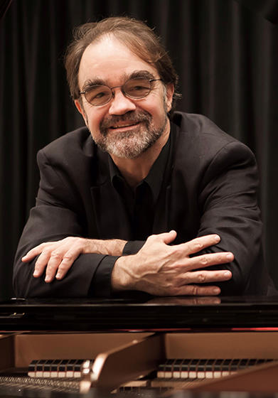 Schar School of Policy and Government professor John S. Earle leans on an open piano.